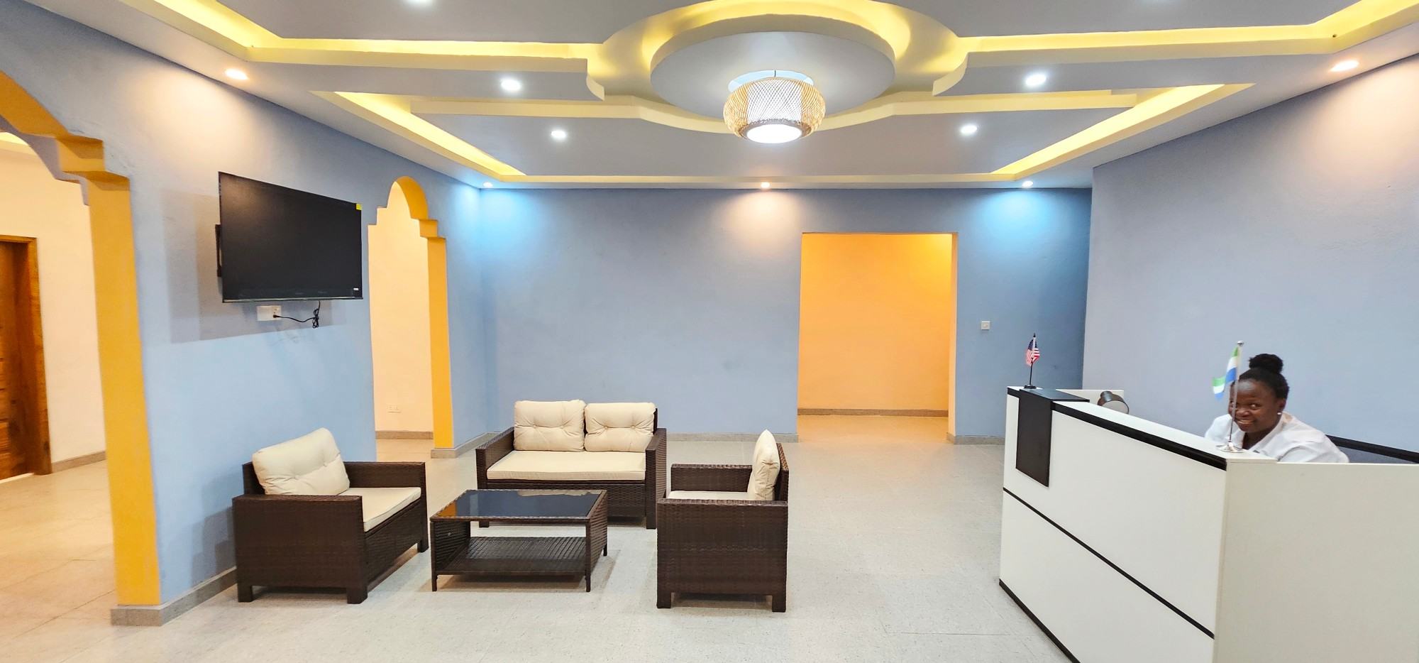 The Africa Waka Waka lobby: rattan sofas under a lit ceiling, and a smiling receptionist at the front desk